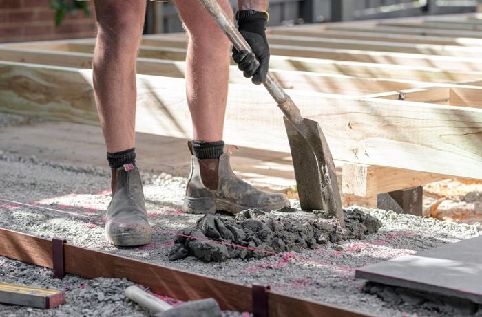 Person laying mortar mix on gravel base using a spade.