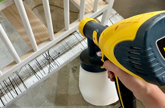 Hand holding paint sprayer on top of white wooden railings in an indoor environment