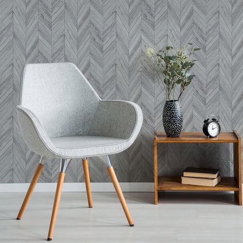 A grey chair with light grey herringbone wallpaper on the wall.