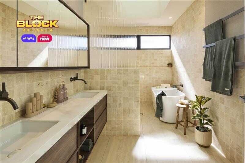 Modern bathroom with beige tiles, white bathtub, black showerhead and knobs, and natural light from a small window. 