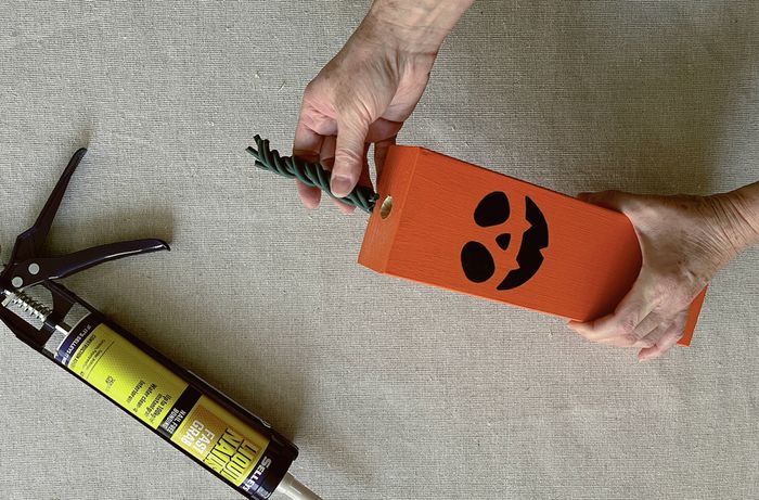 A hand inserting a hex head bolt into a drilled hole in a orange block, with a cartridge of adhesive nearby.