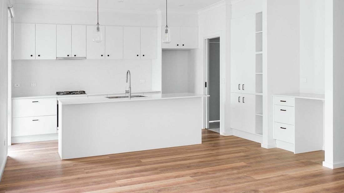 A wide shot of a new white kitchen installation with black handles and two glass light-bulb centrepieces hanging from the ceiling.