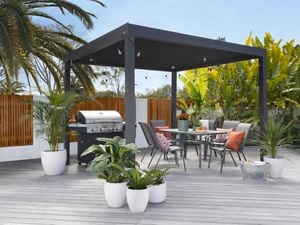 Gazibo with outdoor chairs, table, plants, barbeque and lights.