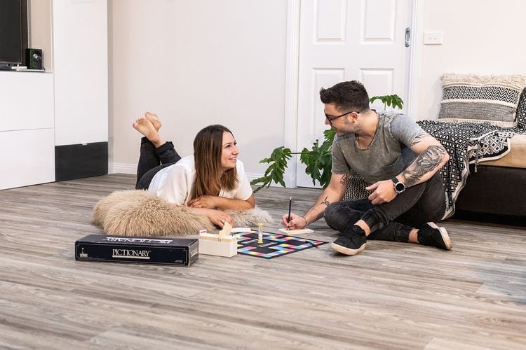 Woman and man sitting on vinyl plank timber-look floor playing a board game