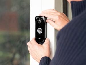 Close-up of a person installing a smart video doorbell on a white door frame, with the camera lens and doorbell button visible beside a glass panel.