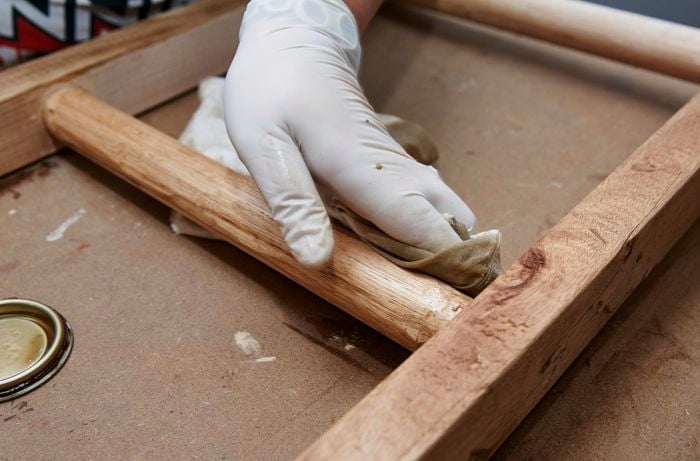 Person wiping DIY timber vintage ladder with rag and varnish.