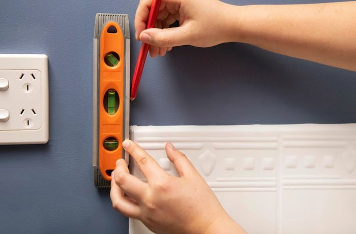 A person marking a line on a wall using a spirit level