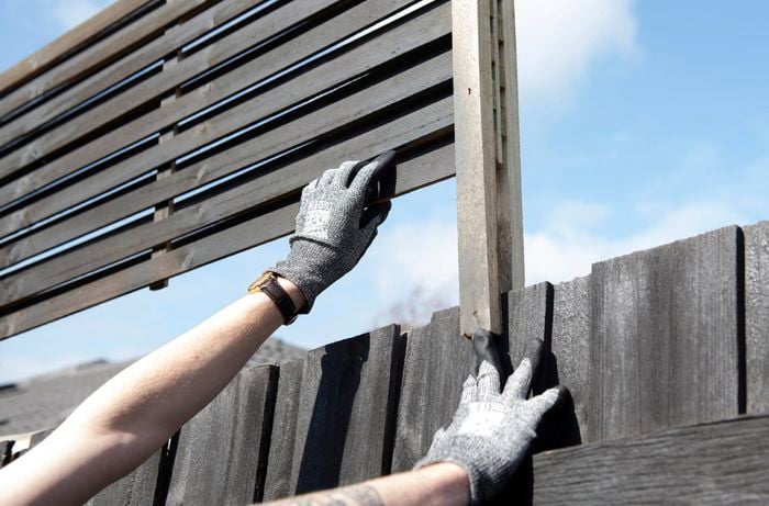 Gloved person attaching a fence extension to a wooden fence