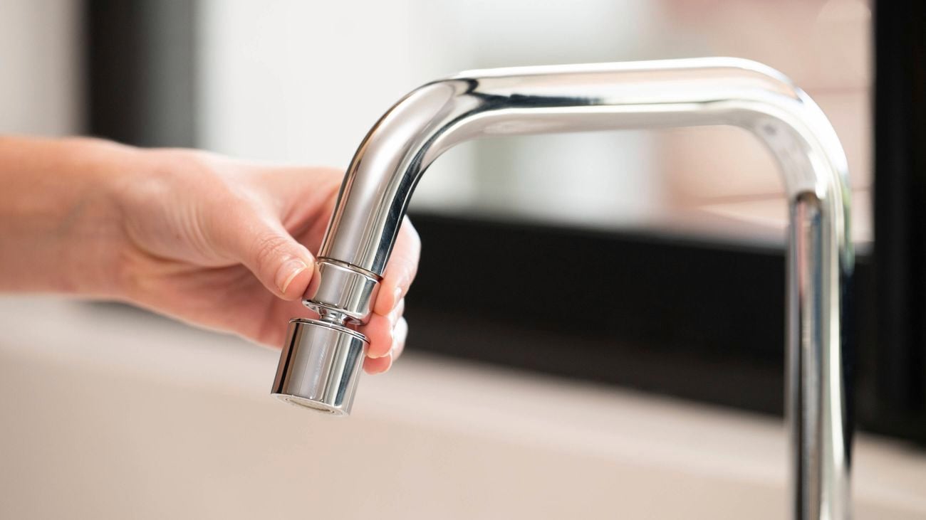 A person is installing a swivel aerator onto a kitchen tap by hand