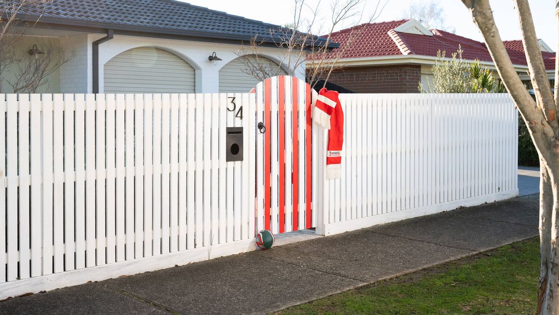 Finished white fence with a red striped gate, scarf and football decorating the entrance.