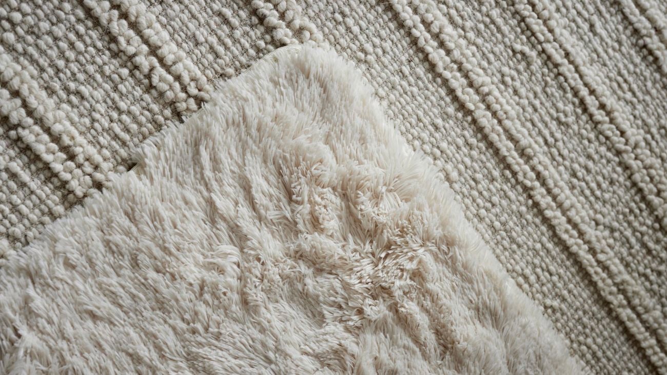 Close-up shot of a white tufted rug layered over the top of a cream bouclé rug.