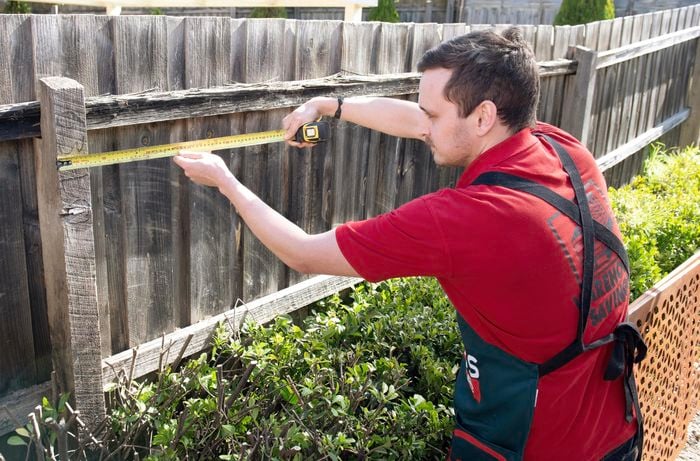 A person measuring the distance from a fence post