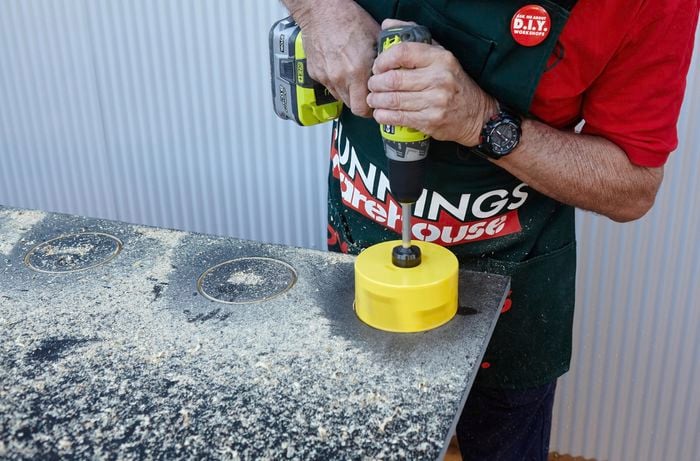 A hole saw being used to cut holes in the vertical garden tier for pot plants to sit in