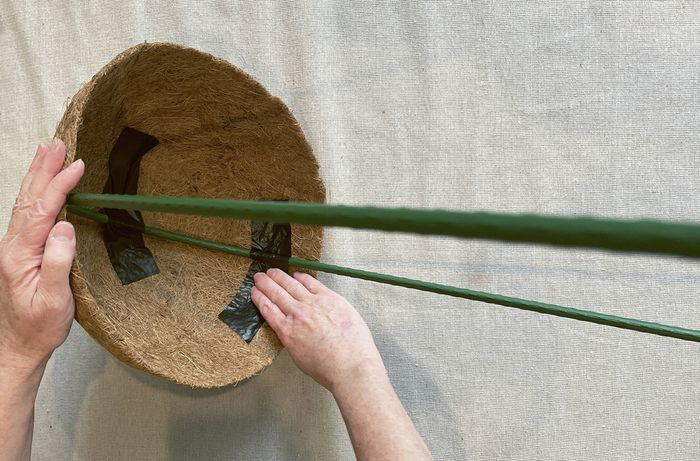 Hands attaching a green garden U hoop to a coir basket with black duct tape.