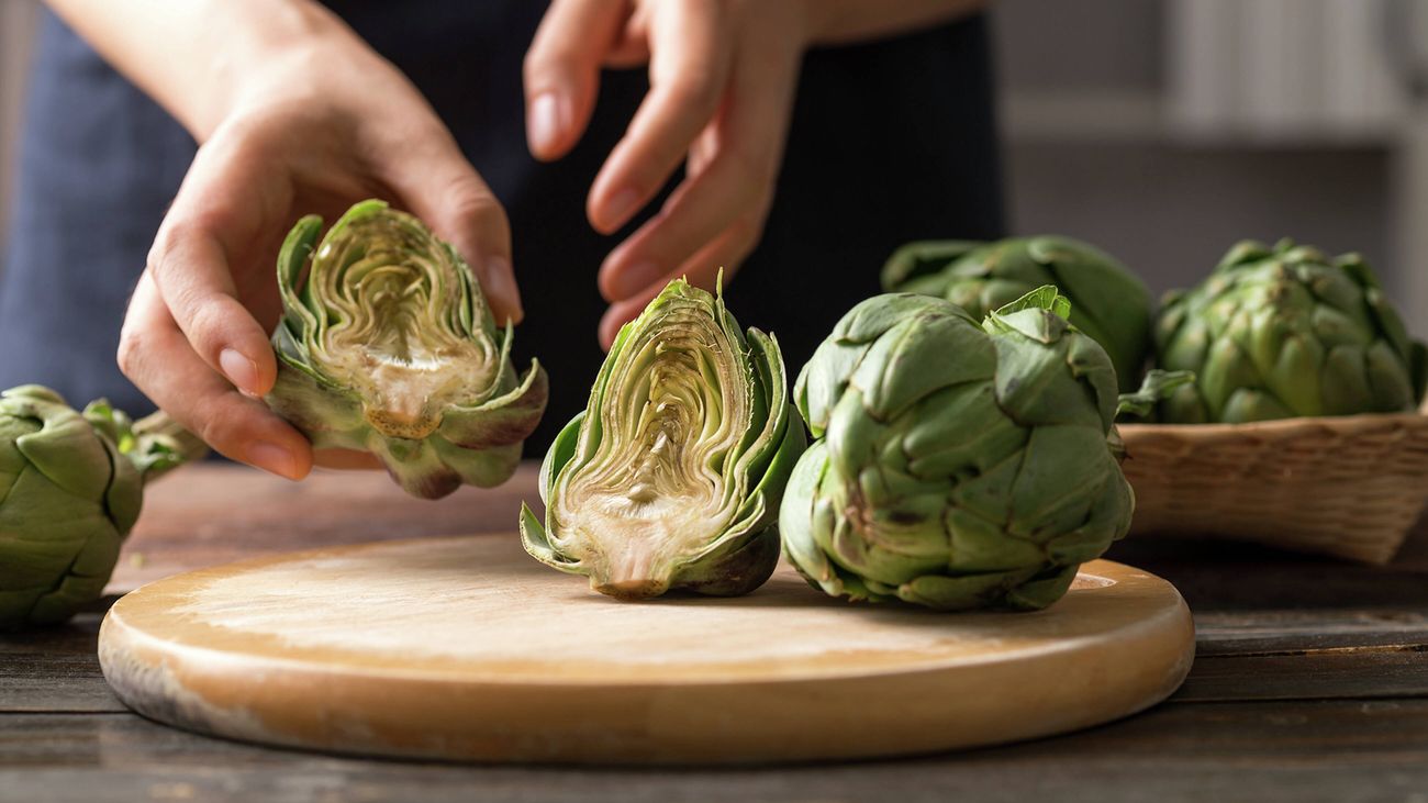 Some artichokes on the kitchen bench with one cut in half on the cutting board