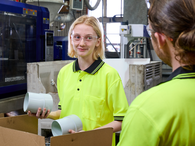 A worker
  in a hi-vis yellow shirt holds two PVC fittings while talking to another
  worker.