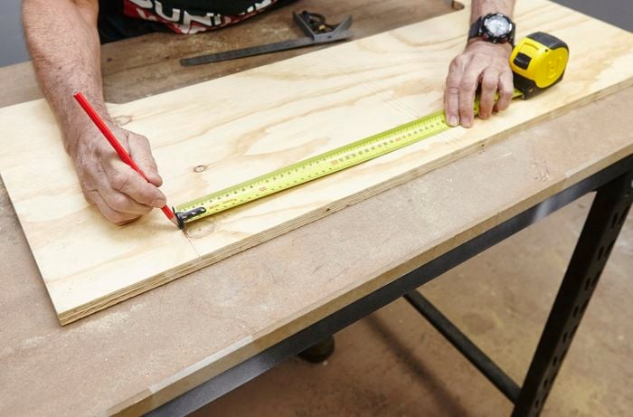 Person measuring and marking ply panel with tape measure and pencil