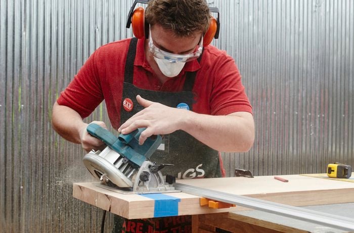 A person cutting a length of hardwood on a 45 degree angle with a circular saw
