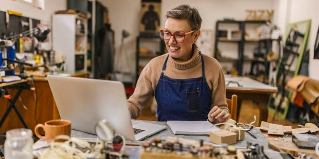 A lady sitting at a desk with a laptop and lots of other items on it.