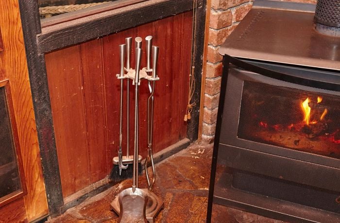 Fire tools including tongs, poker sticks, a shovel and a brush next to a wood heater 