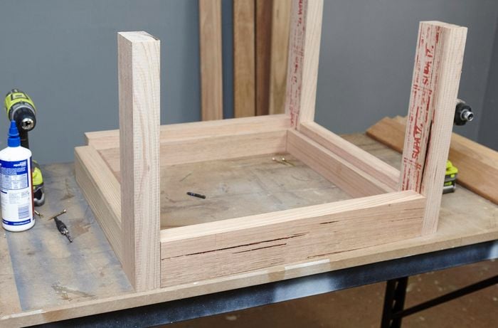 An unassembled wooden table, with a leg yet to be laid out, on a workbench