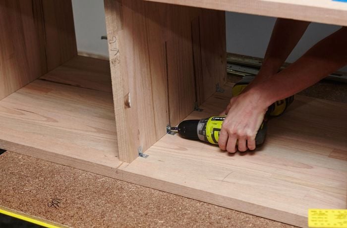 A person attaching a corner bracket onto a shelf inside a timber vanity unit