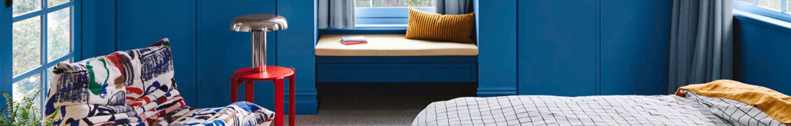 Bedroom painted in blue with a red table lamp in frame