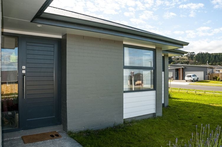 Exterior of a brick house painted mid-grey with a dark grey front door