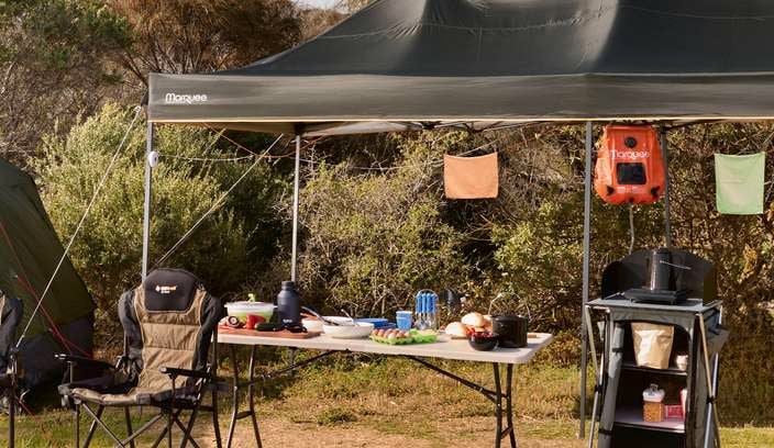Camping tent, gazebo, chairs, table, esky and camping gear in park site outdoors