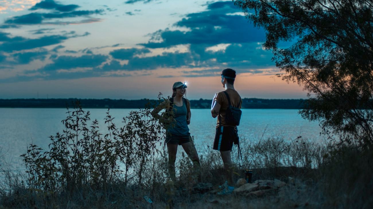 Two people standing by the water at dusk wearing a headlamp