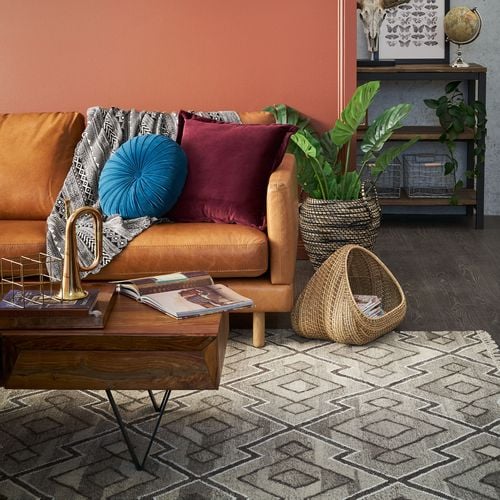 Detail of retro style living room painted terracotta with tan leather couch and patterned rug