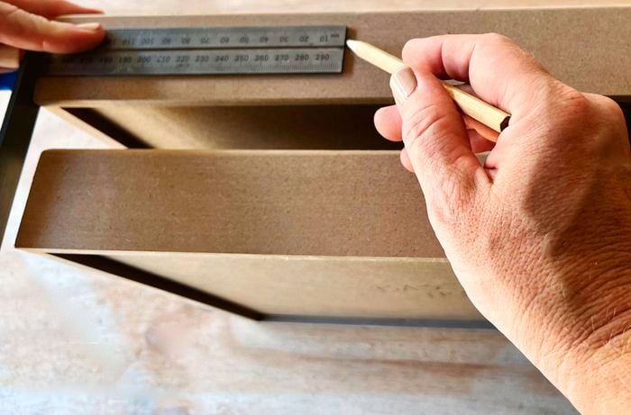 A person marks an MDF tray using a ruler and a pencil.