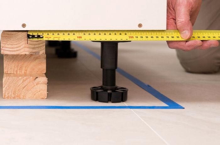 A person is using a measuring tape to measure the distance from the front edge of each cabinet to the timber support frame underneath