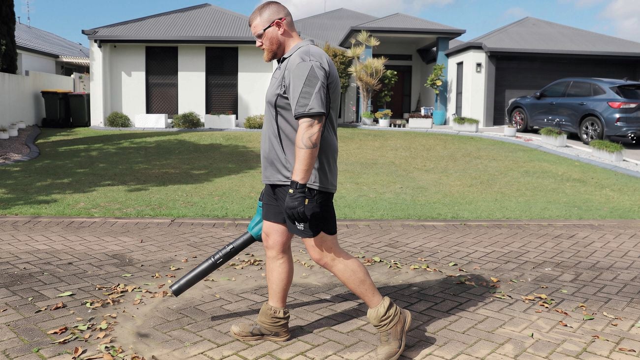 Person using a leaf blower to clear leaves and debris from a driveway.
