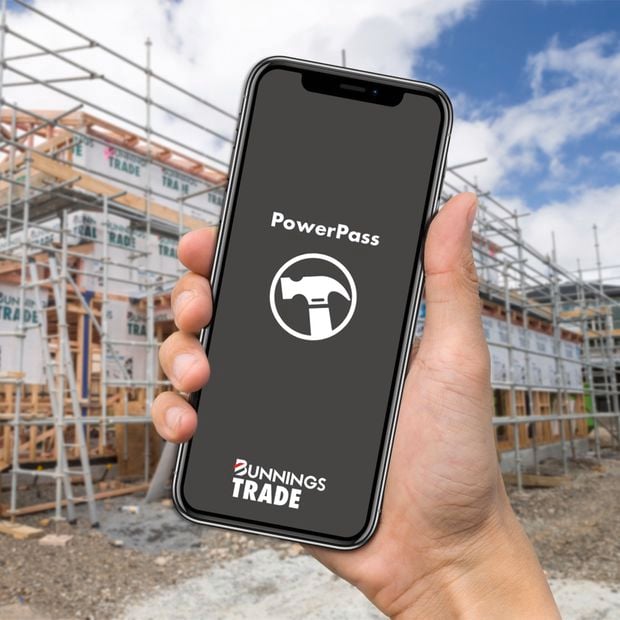 A hand holding a phone with the PowerPass app open on a construction site