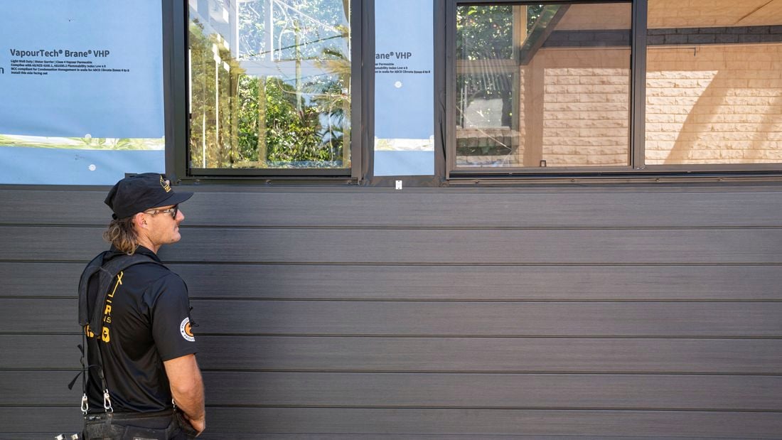 A young builder standing beside a tiny house exterior wall clad in Ekodeck Shiplap Cladding