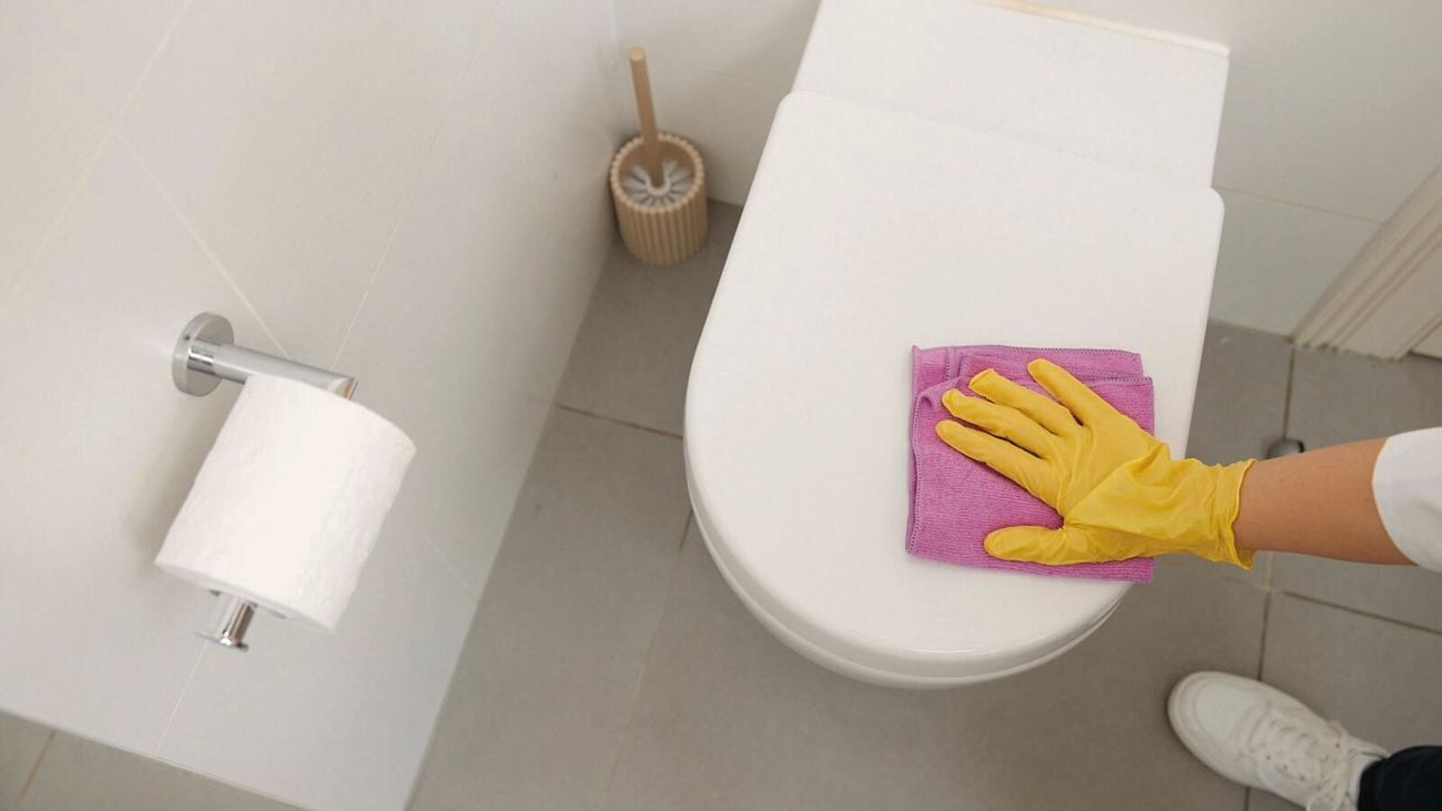 Hand in yellow glove uses pink cloth to wipe toilet.