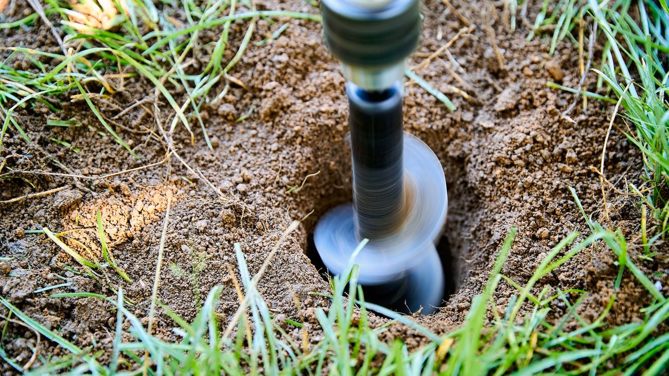 Close-up of a rotating drill auger boring a hole into the ground, with grass around the opening