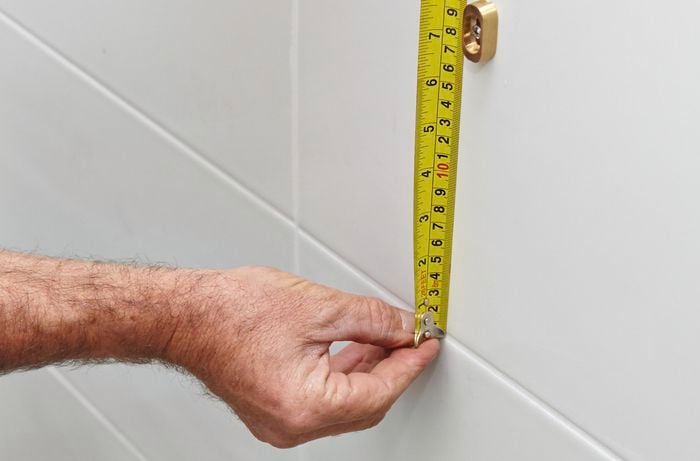 A person measuring a white tiled wall