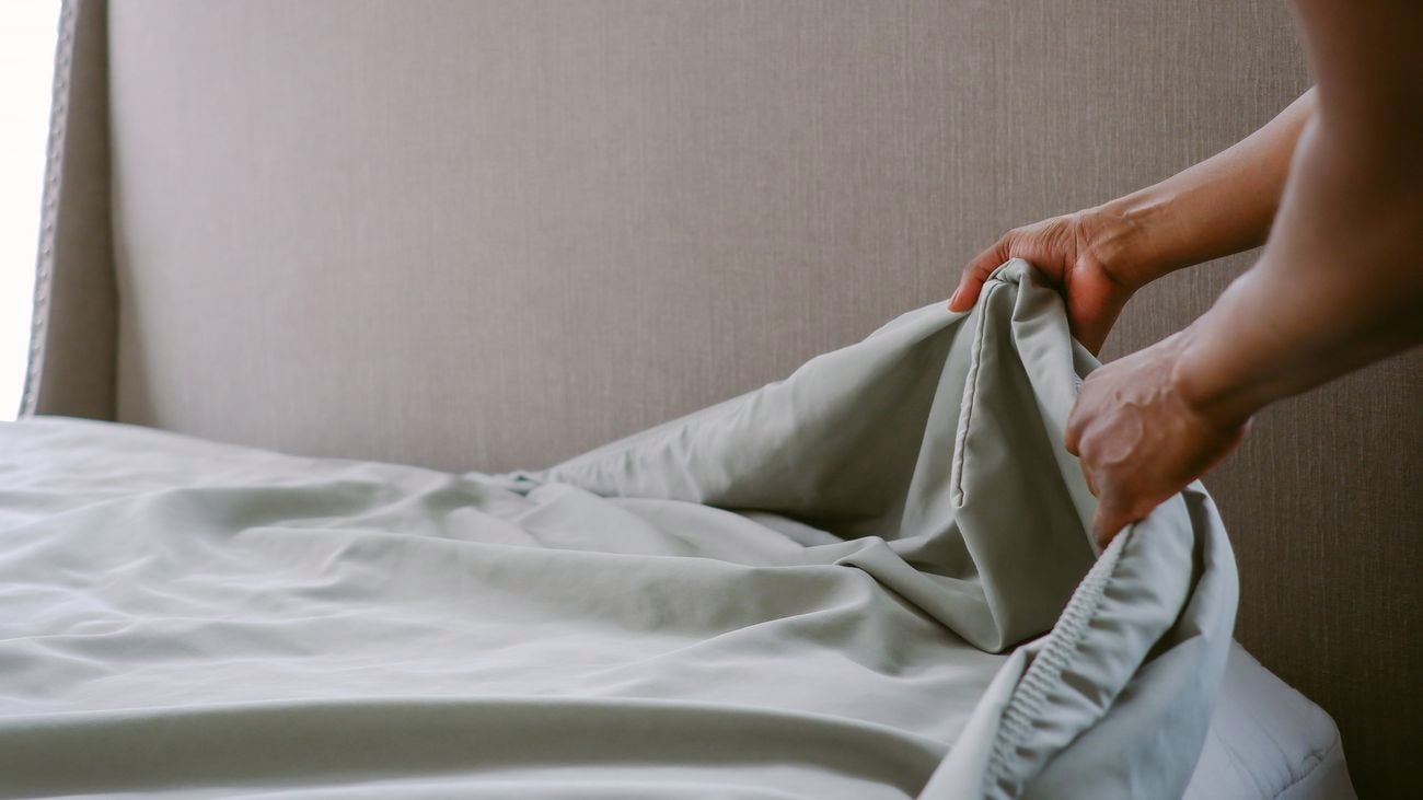 Close-up of hands putting freshly laundered sheet on bed