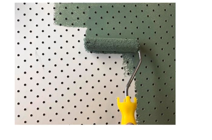 Person painting pegboard wall with paint roller.