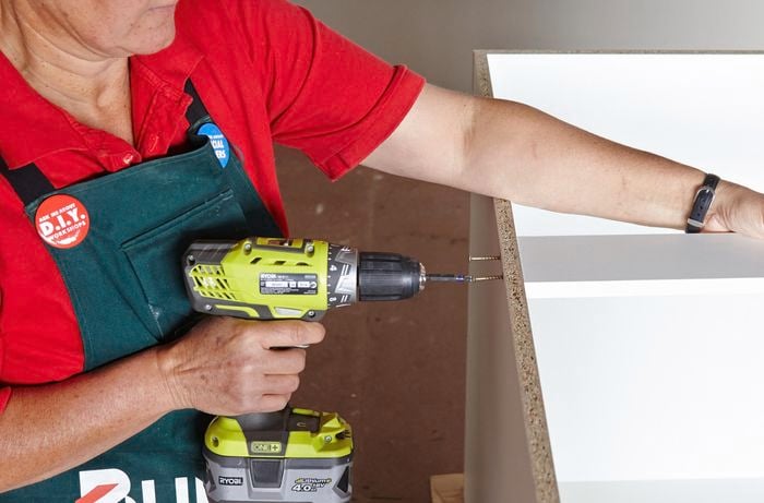 Person drilling screw into panel of cabinet
