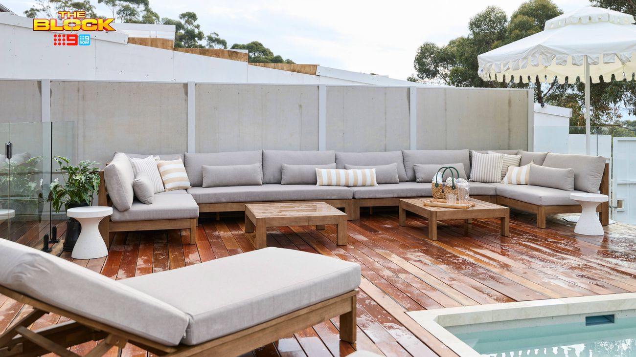 Outdoor poolside entertaining area featuring grey modular sofas, timber decking, coffee tables and a white umbrella.