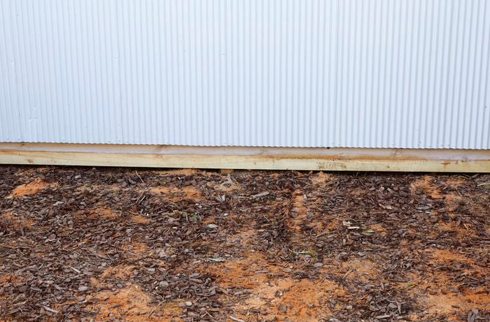 A bare patch of ground in front of a corrugated iron wall, ideal for a sleeper compost bin