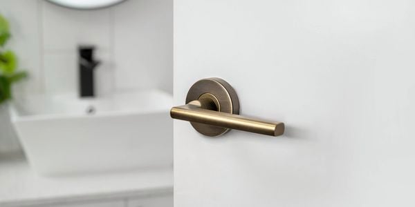 A Delf Madrid Lever Set Antique Brass door handle on a white door to a bathroom