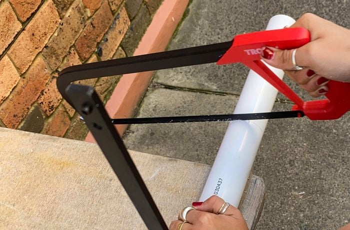 A pair of hands cutting a PVC pipe