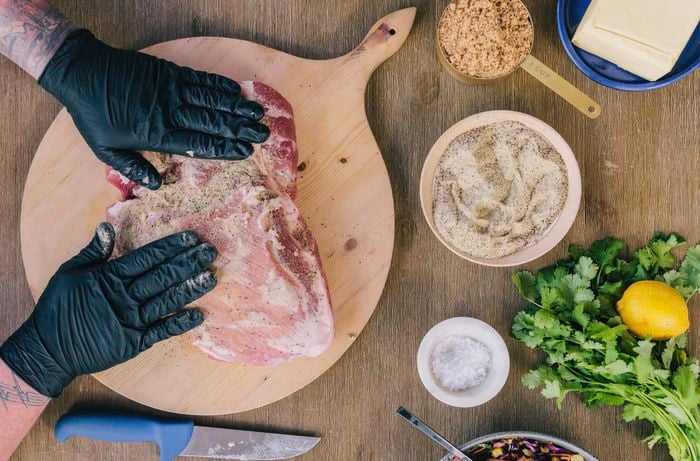 Person rubbing spice mix into a pork shoulder