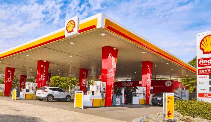 A shell petrol station with two cars parked in it.