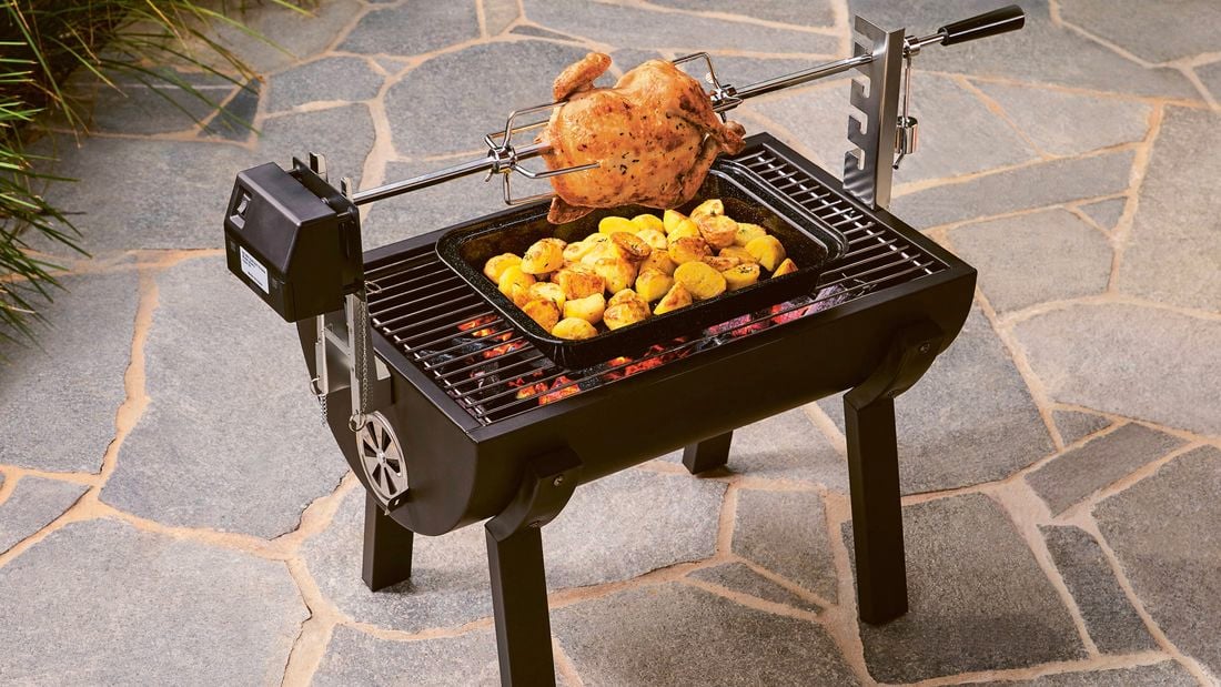 Charcoal chicken and roasted potatoes cooking on a rotisserie grill on a patio.