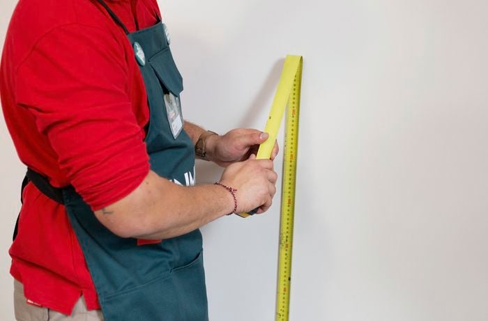 Person using measuring tape and bending it against a wall.